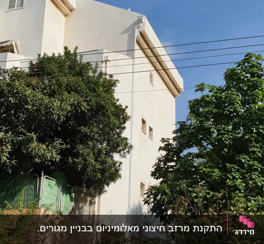 בניין לבן עם עצים וענפים מסביב